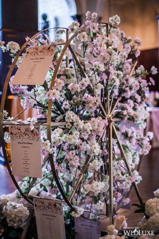 In questa foto un tableau di nozze originale a forma di ruota panoramica decorata con fiori di colore rosa e bianco