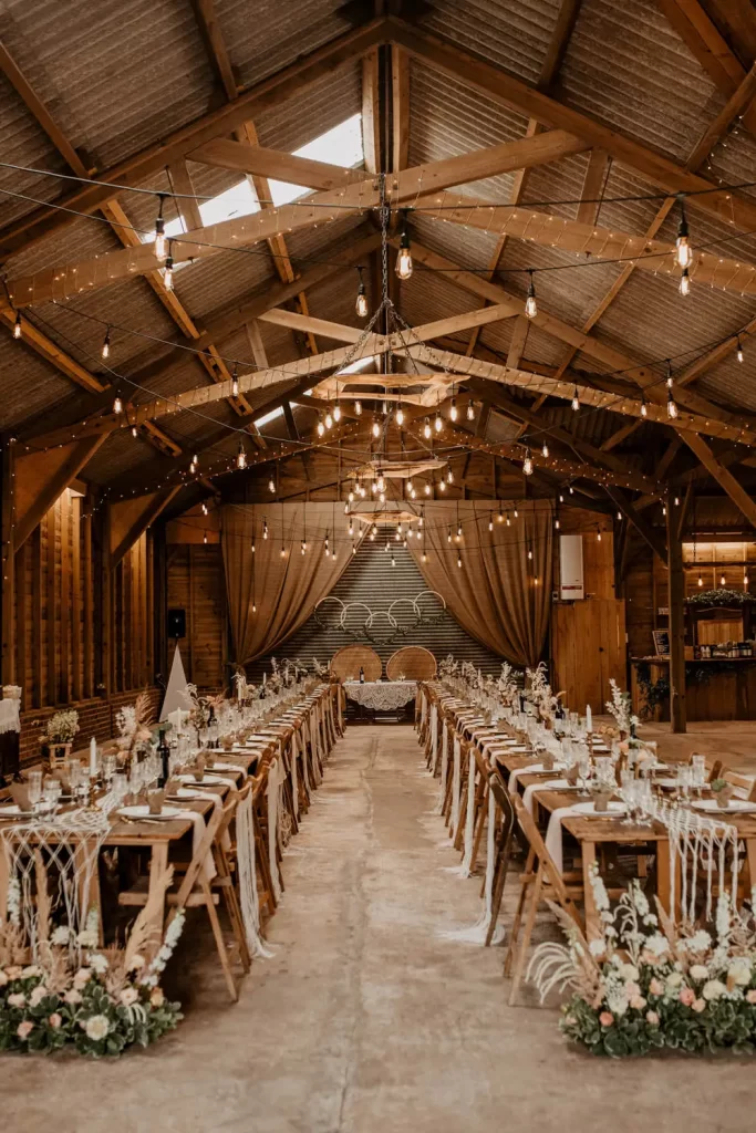 In questa foto due tavoli per matrimonio imperiali in legno nudo visti frontalmente e allestiti in stile Boho Chic all'interno di una sala in legno