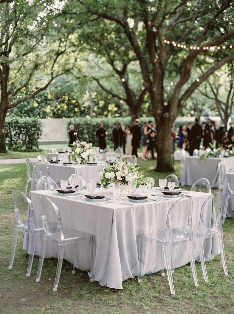 In questa foto un tavolo quadrato allestito in stile elegante con sedie in plexiglass, tovagliato e fiori colore bianco
