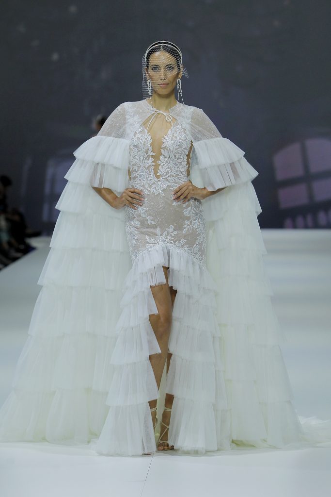 In questa foto la modella indossa un abito da sposa con mantella lunga con balze.