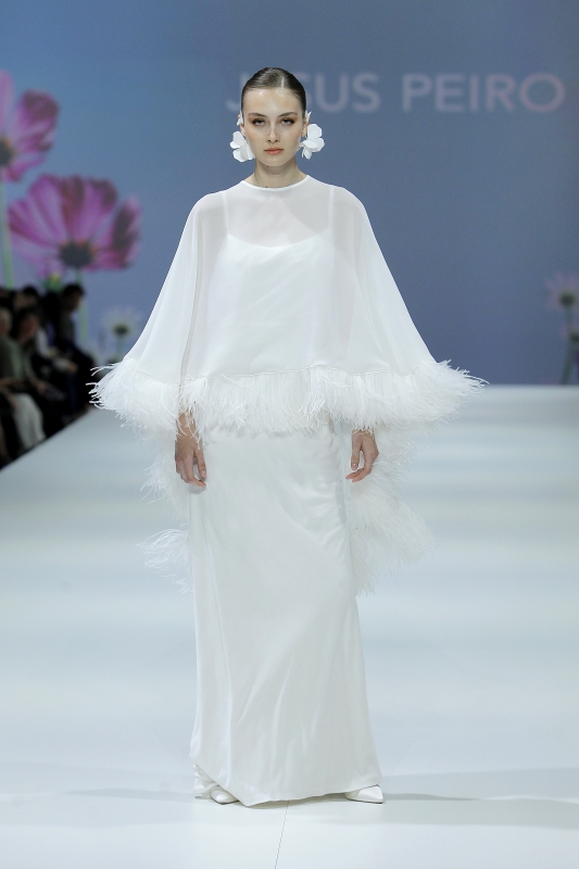 In questa foto la modella indossa un abito da sposa aderente con cappa con piume 2023.
