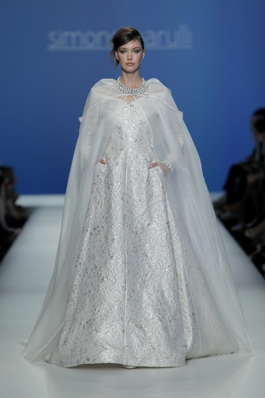 In questa foto la modella indossa un abito da sposa con mantella lunga 2023 Simone Marulli sui toni dell'argento.