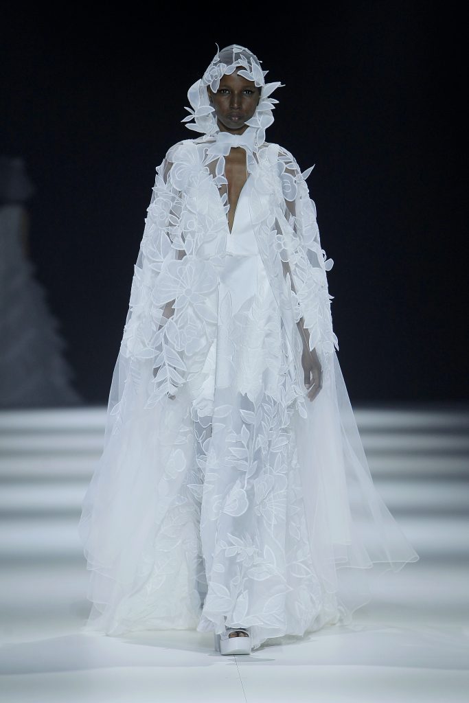 In questa foto la modella indossa un abito da sposa con mantello e cappuccio 2023 con decori floreali.