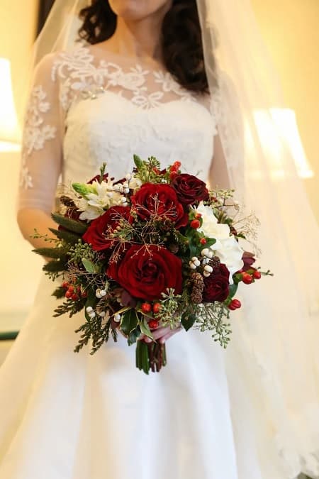 In questa foto, un bouquet natalizio realizzato con rose bianche e rosse, pigne e bacche