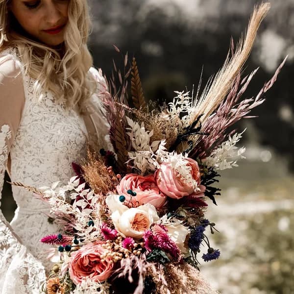 In questa foto, una sposa con in mano un bouquet scomposto sui fiori del rosa, foglie e spighe 