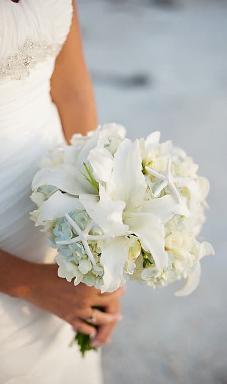 Nella foto, un bouquet rotondo total white con ortensie, gigli e stelle marine 