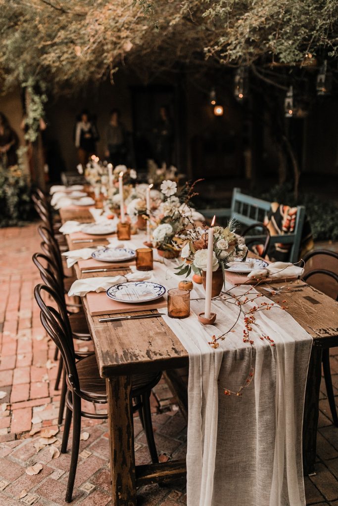 In questa foto un'idea di allestimento boho chic con un tavolo imperiale decorato con un runner colore panna, bicchieri colore marrone, vasi abbinati e fiori colore bianco e beige