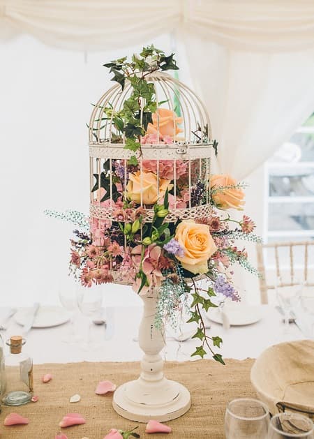 In questa foto, una decorazione floreale sui toni del rosa e dell'arancione è sistemata all'interno di una gabbia bianca