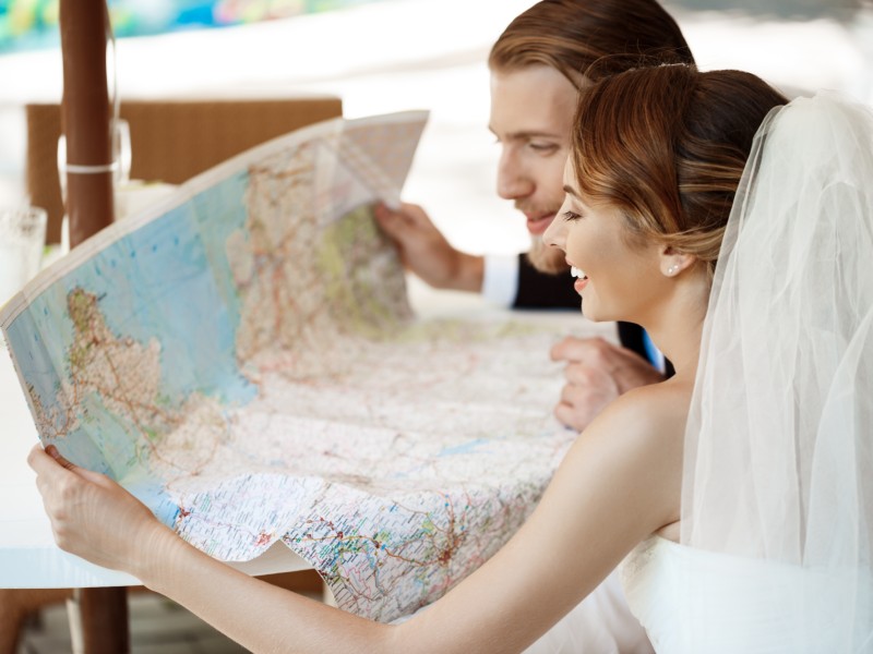 In questa foto due sposi sorridono mentre guardano una cartina geografica prima di raccogliere i documenti viaggio nozze