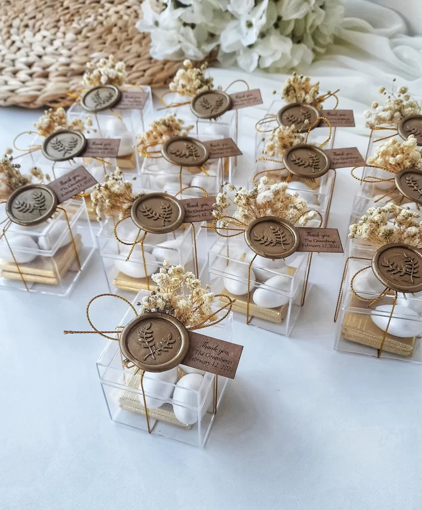 In questa foto un'idea per bomboniera matrimonio con una scatolina trasparente portaconfetti chiusa da un bollino di ceralacca e fiori essiccati