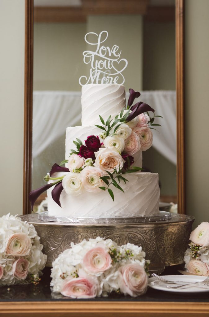 In questa foto una torta di matrimonio  decorata con cake topper di colore bianco e fiori colore bianco, rosa e rosso