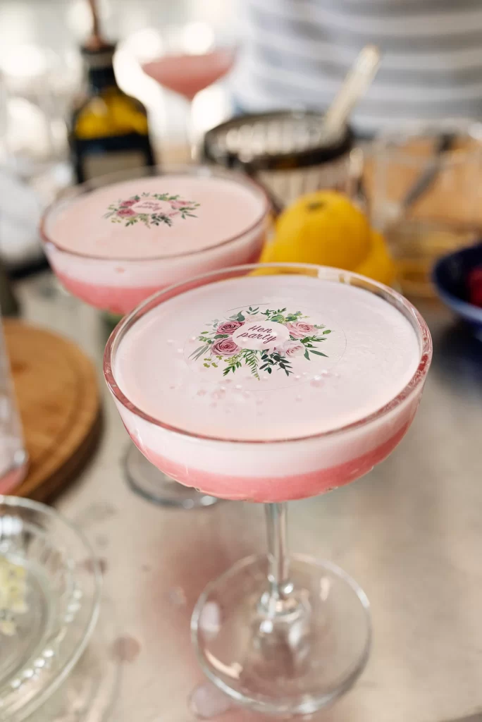 In questa foto cocktail di colore rosa con un topper personalizzato con il loro degli sposi