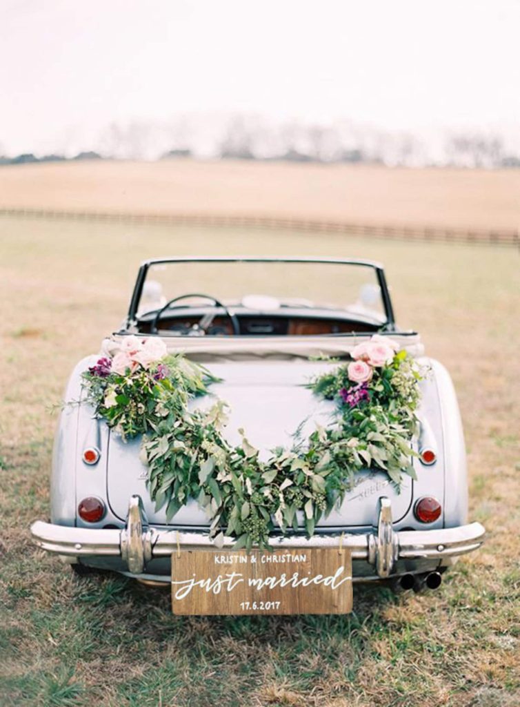 In questa foto un'auto per gli sposi decorata con fiori, foglie e una targa personalizzata con i nomi e la data delle nozze, tra le idee originali per matrimonio