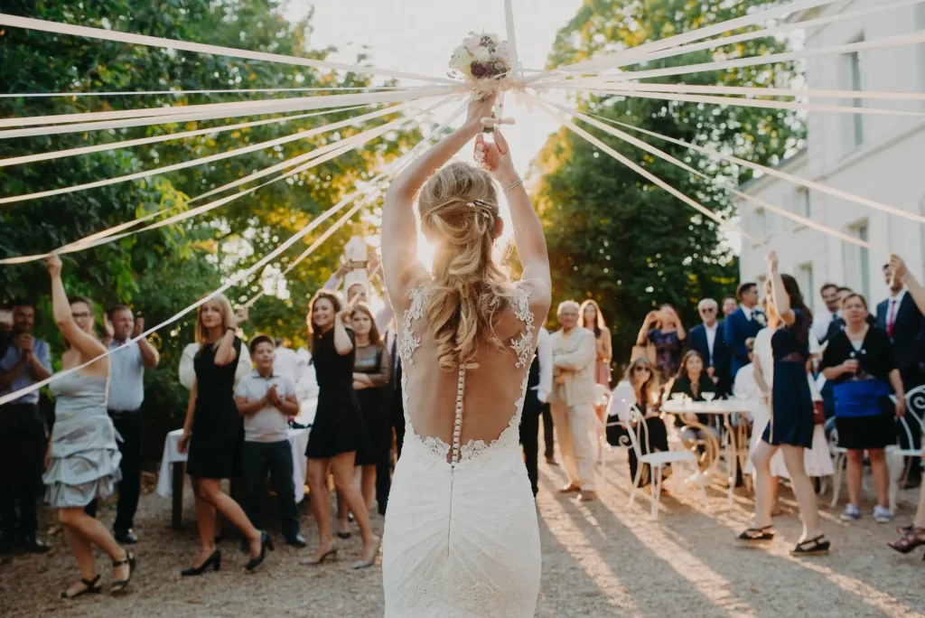 In questa foto una sposa di spalle tiene un bouquet con nastri attaccati