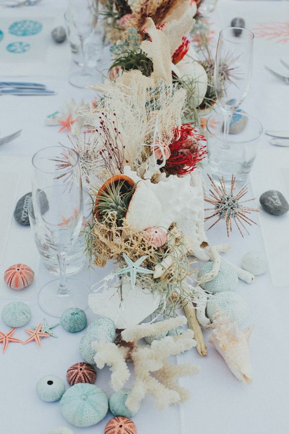 In questa foto un'idea di centrotavola matrimonio a tema mare con conchiglie, alghe, coralli e sassolini