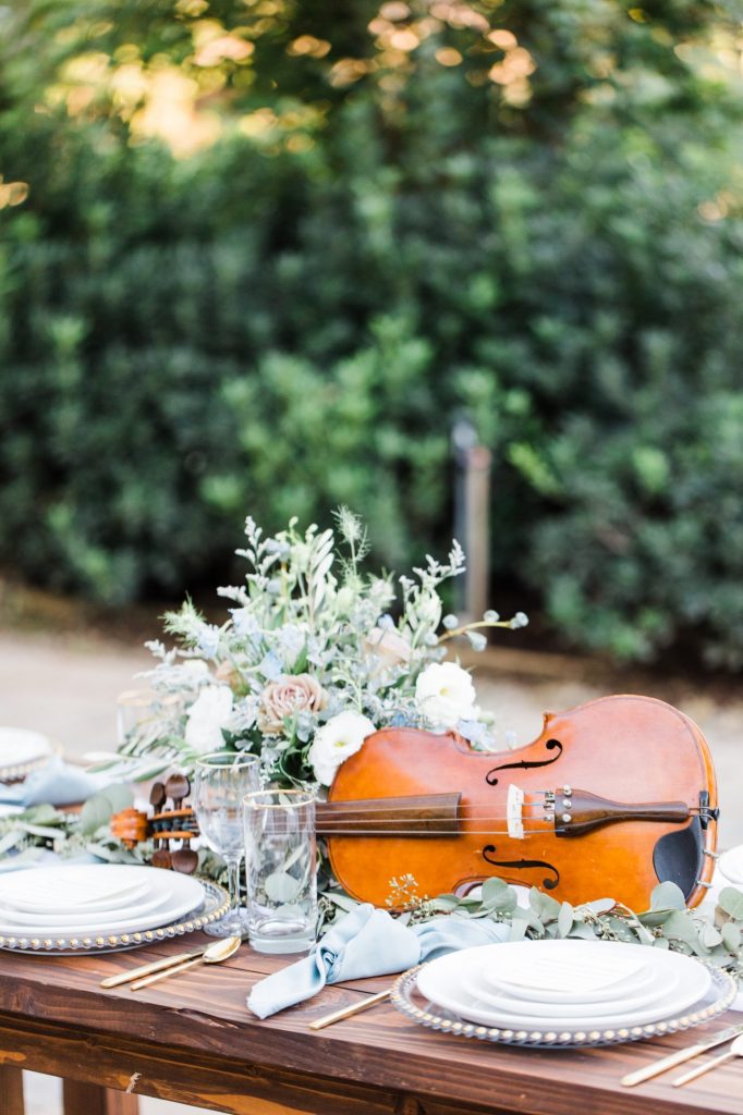 In questa foto un'idea di centrotavola matrimonio a tema musica con un violino e fiori nei colori del bianco e del beige
