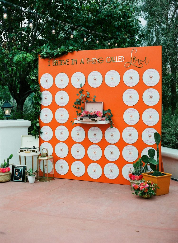 In questa foto un'idea di tableau mariage a tema musica con dischi di vinile di colore bianco disposti su un pannello colore arancio. Su ogni disco sono scritti i nomi degli ospiti