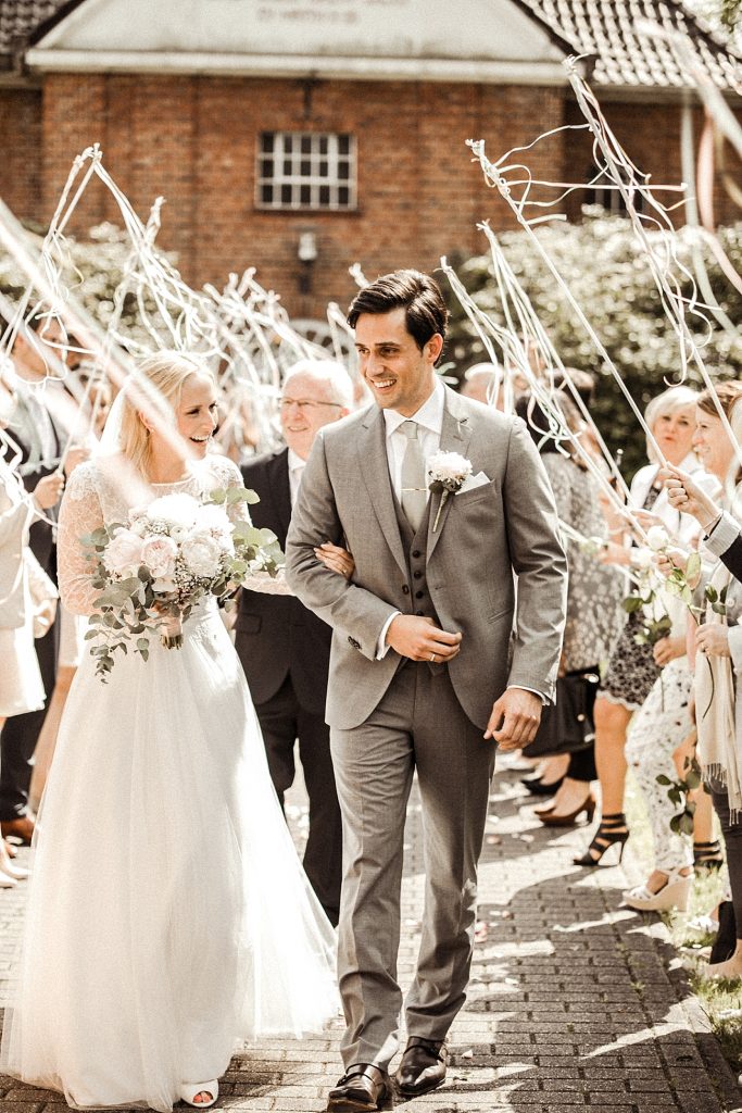 In questa foto idee matrimonio per l'uscita dalla chiesa: gli sposi camminano sorridenti tra gli ospiti che agitano le wedding wands, cioè le bacchette con nastri colorati attaccati