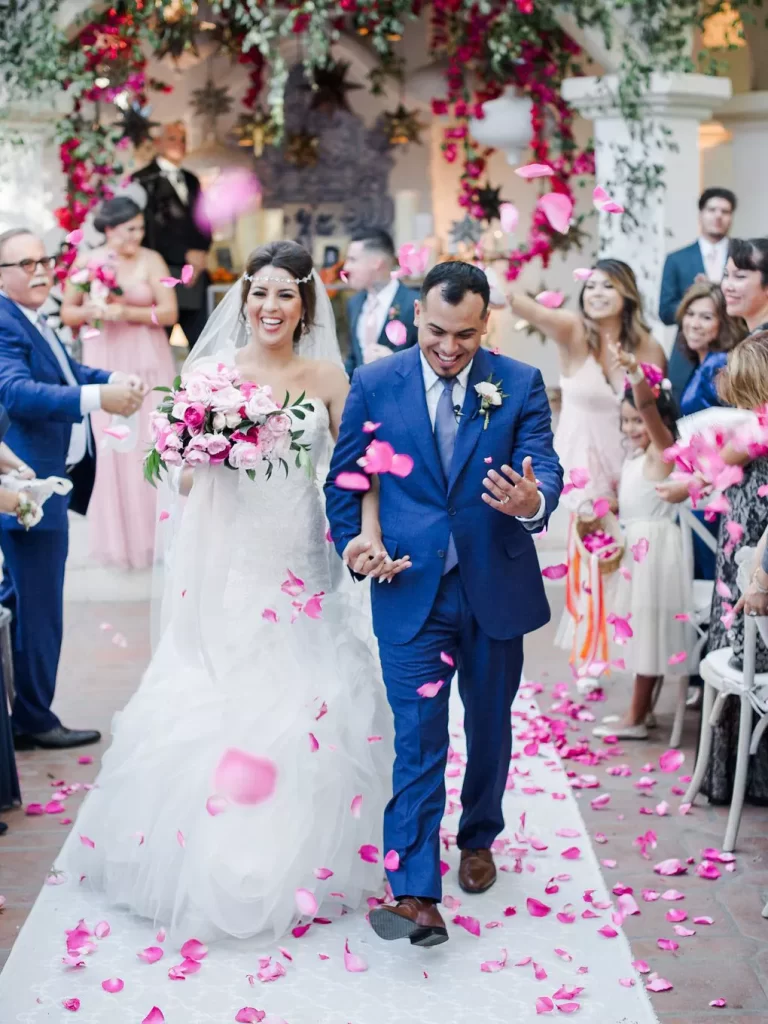In questa foto idee matrimonio per l'uscita dalla chiesa: due sposi camminano tra gli ospiti che lanciano petali di rosa fucsia