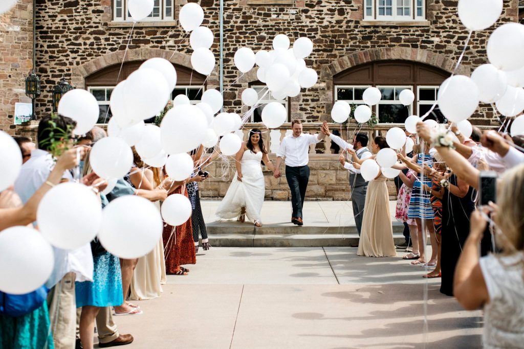In questa foto idee matrimonio per l'uscita dalla chiesa: due sposi camminano tra gli ospiti che tengono in mano palloncini bianchi