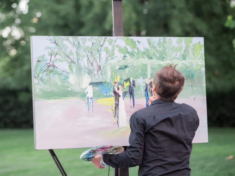 In questa foto di intrattenimento matrimonio un pittore di Live Painting è ritratto di spalle mentre dipinge la scena di due sposi che ballano al centro della pista