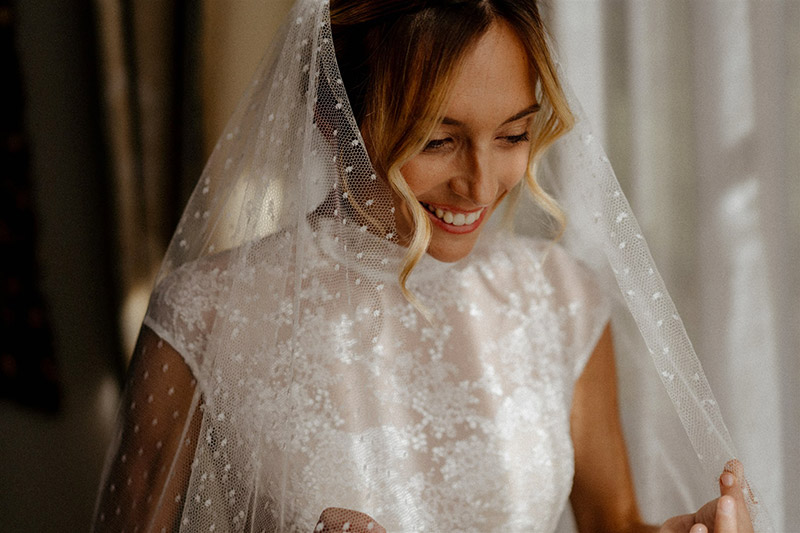 In questa foto una sposa sorridente indossa un abito da sposa Giuliani Couture in pizzo e un lungo velo