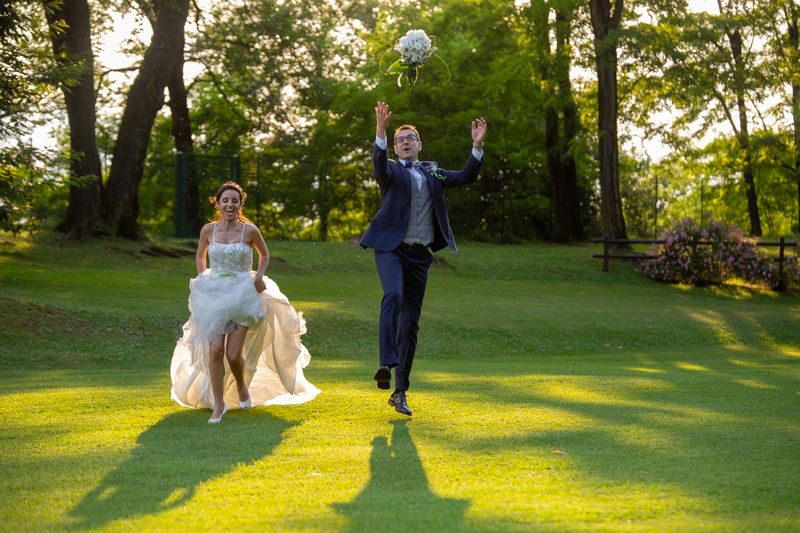 in questa foto una coppia di sposi allegri, fotografati mentre insieme corrono in un prato verde