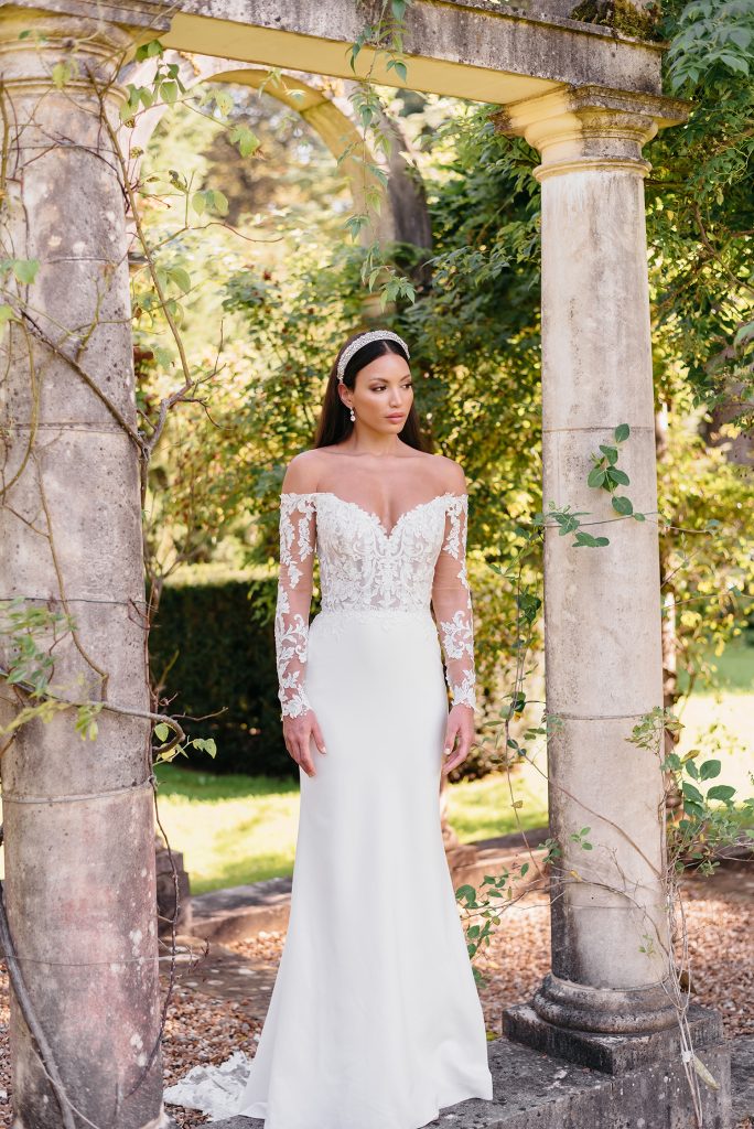 In questa foto un abito da sposa semi sirena di Justin Alexander con maniche e corpetto steccato decorati con ricami in pizzo floreale intessuto di fili d’argento