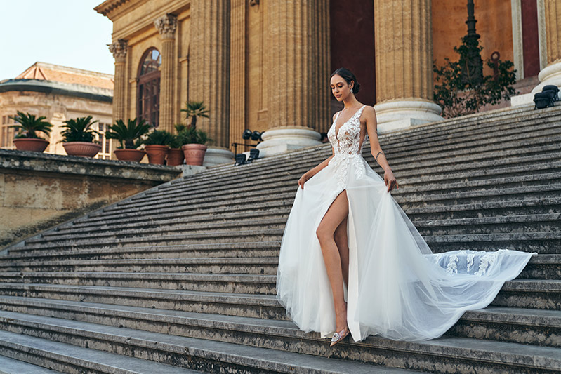 In questa foto una modella scende la scalinata del Teatro Massimo di Palermo mentre indossa un abito da sposa a A Annais Bridal 2023 con gonna in tulle con spacco e corpetto a V con ricami di pizzo floreale