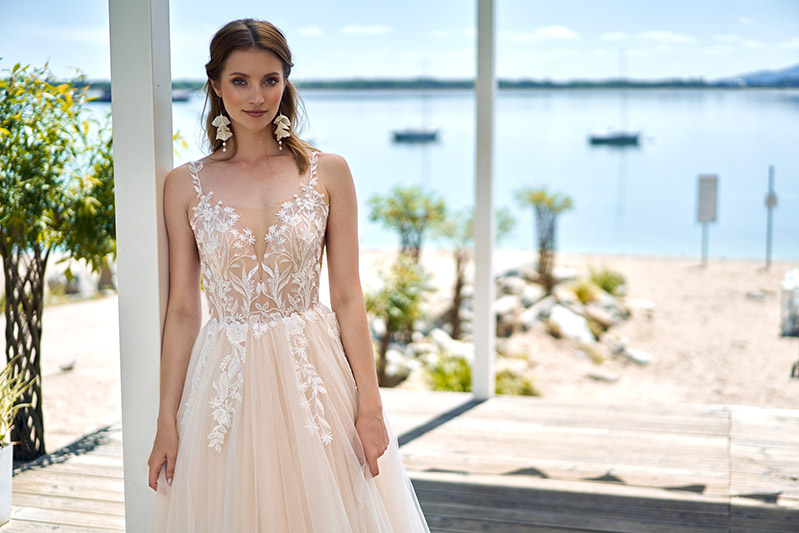 In questa foto una modella indossa uno degli abiti da sposa Annais Bridal 2023 in tulle colore cipria con corpetto ricamato, scollatura illusion e ramage sul punto vita
