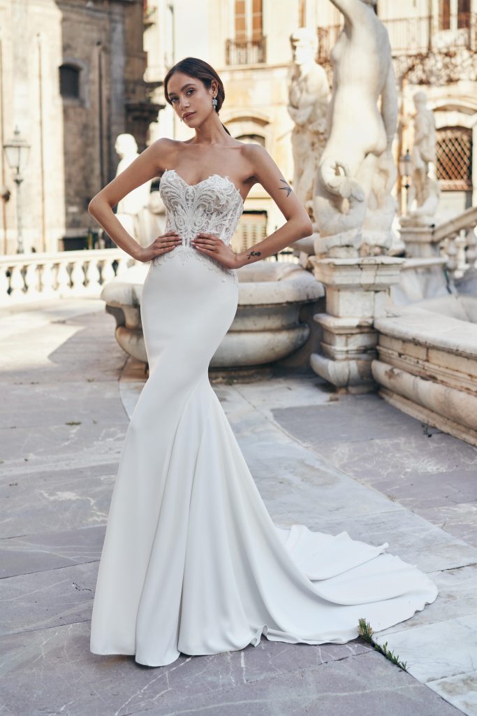 In questa foto una modella indossa un abito da semi sirena di Annais Bridal 2023 con gonna in crêpe georgette e bustier in pizzo con scollo a cuore senza spalline