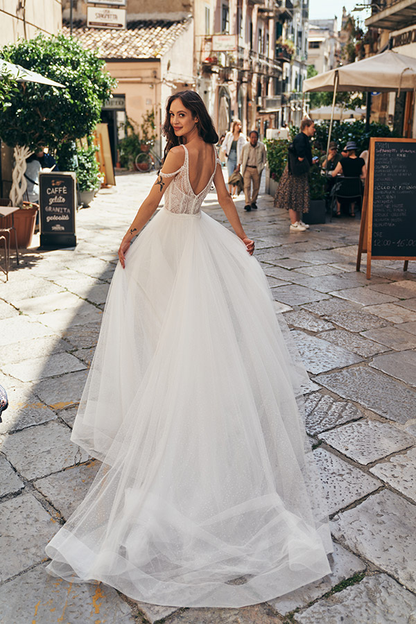 In questa foot una modella cammina per strada e mentre si gira mostra uno degli abiti da sposa Annais Bridal 2023 con gonna e strascico in tulle e schiena scoperta