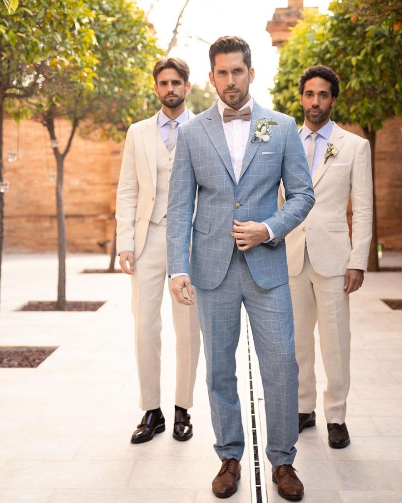 In questa foto tre modelli indossano abiti da sposo chiari di Hockerty. Il modello in primo piano indossa un vestito di colore azzurro polvere, i due modelli in secondo piano due abiti di colore beige