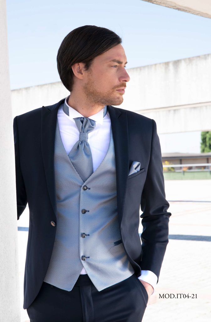 In questa foto un modello indossa un abito da sposo classico di colore blu scuro con gilet a contrasto di colore grigio abbinato alla pochette nel taschino di Luigi Convertini