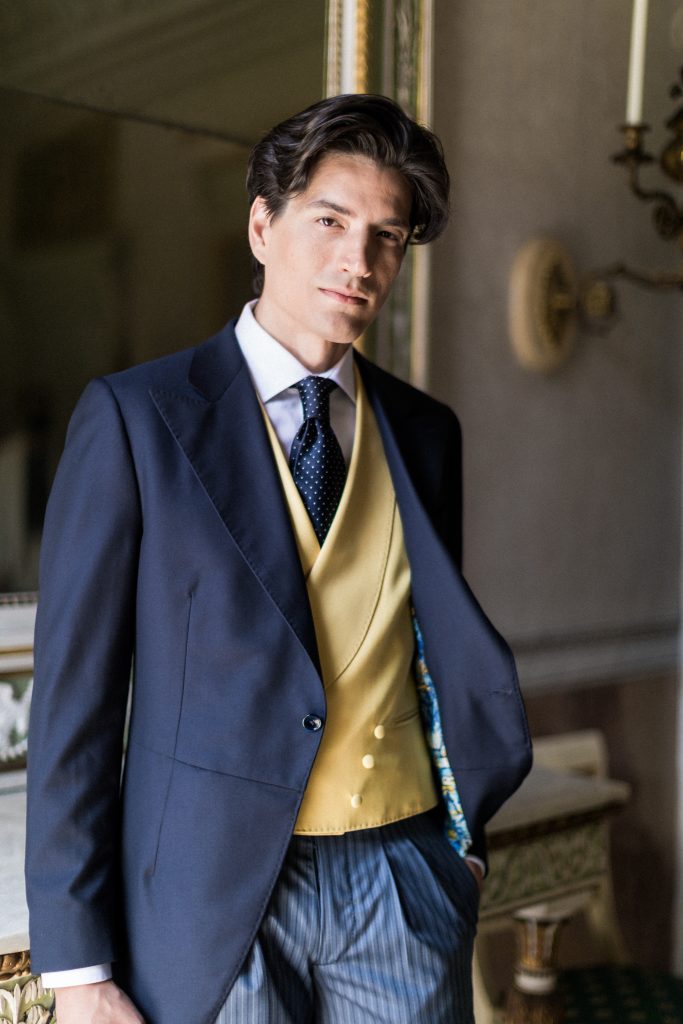 In questa foto un modello indossa un abito da sposo spezzato con giacca di colore blu, gilet di colore giallo, pantaloni a righe di Sanvenero