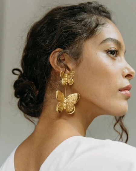 In questa foto una modella indossa degli orecchini a forma di farfalla d'oro con l'abito da sposa.