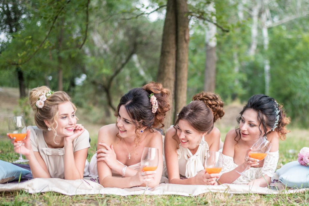 In questa foto quattro ragazze sdraiate su un prato ridono tenendo in mano un bicchiere di succo di frutta alla fine di un picnic