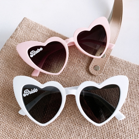 In questa foto due occhiali da sole a forma di cuore di colore bianco e rosa per addio al nubilato