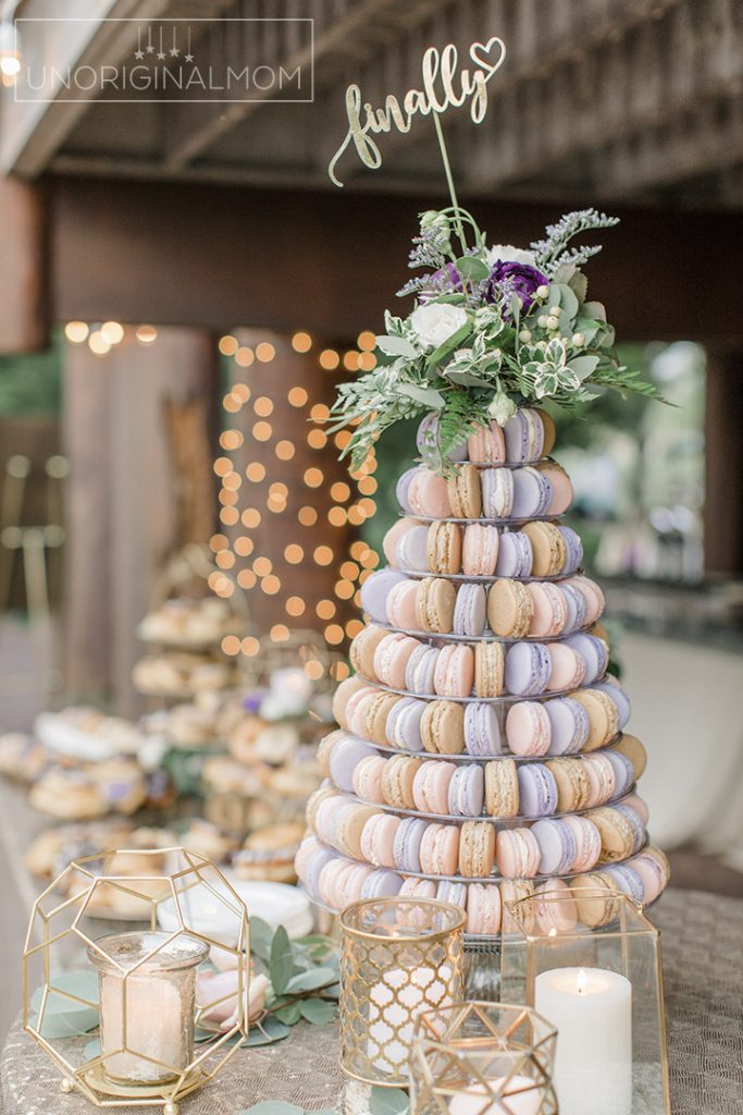 In questa foto una torre di macarons nei colori del lilla e rosa con cake topper con la parola Finally