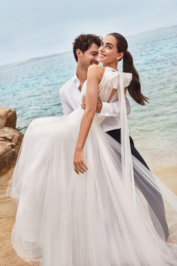 In questa foto uno sposo prende in braccio una sposa che guarda verso l'alto. È mostrato il fiocco in tulle che scende lungo la schiena