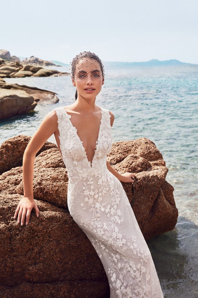 In questa foto una modella in riva al mare indossa un abito da sposa semi sirena in pizzo  
