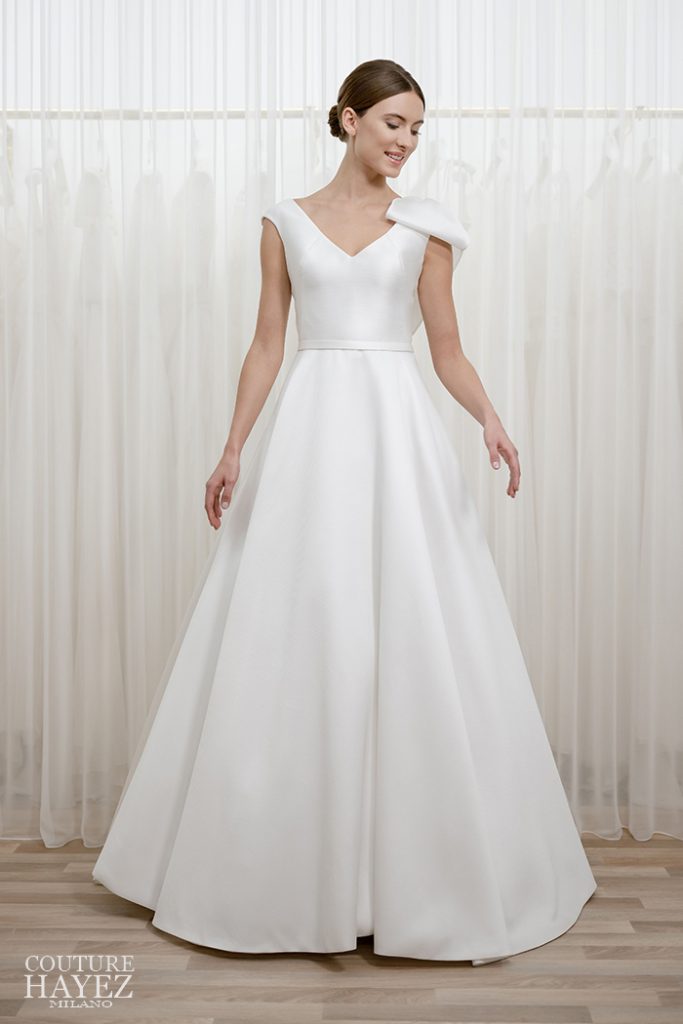 In questa foto una modella indossa un abito da sposa ad A in mikado con fiocco monospalla di Couture Hayez