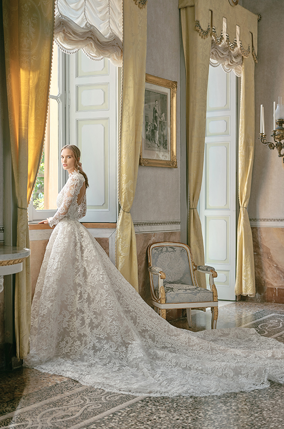 In questa foto una modella di spalle indossa un abito a trapezio con lunga in pizzo di Monique Lhuillier. Sulle spalle si intravede una scollatura circolare 