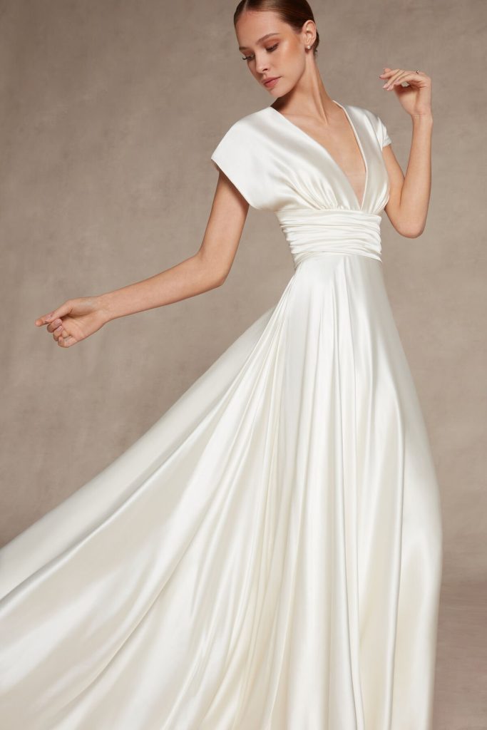 In questa foto una modella indossa un abito da sposa in seta con scollo a V e manichette di Atelier Emé