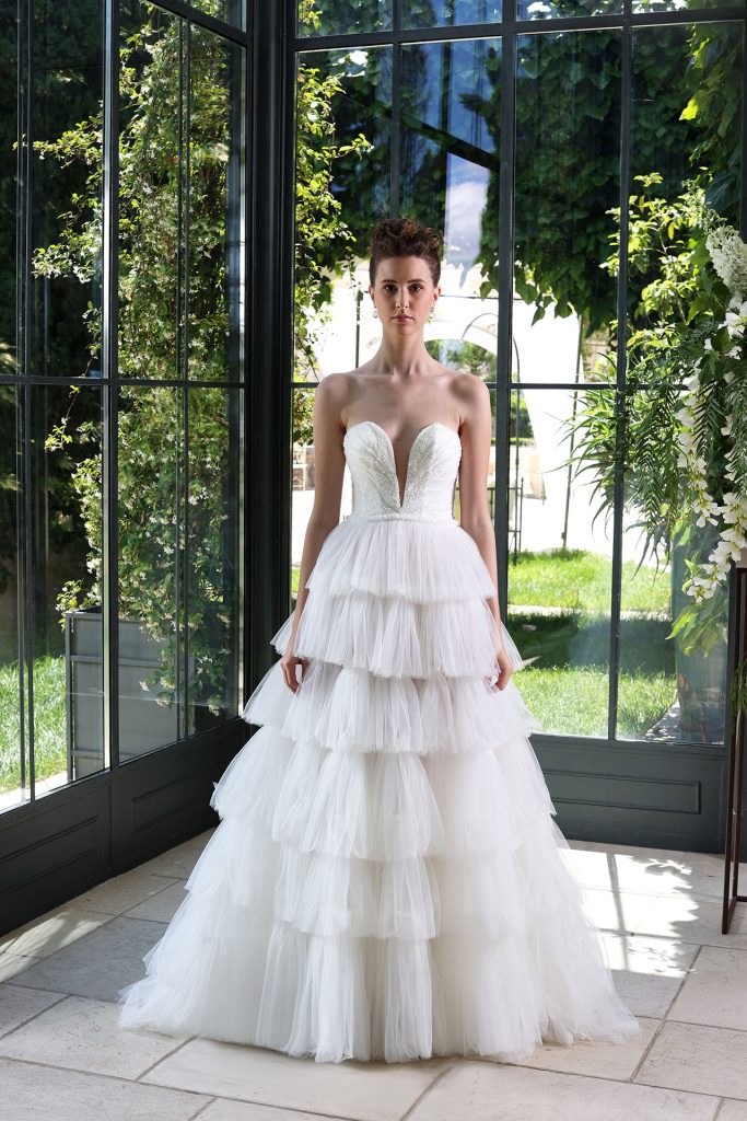 In questa foto un modella indossa un abito da sposa a balze in tulle con scollo a V di Enzo Miccio