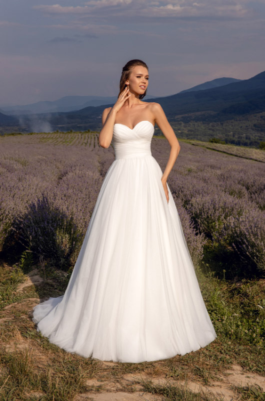 In questa foto una modella in un campo di lavanda indossa un abito da sposa in tulle, con scollo a cuore, della collezione 2023 di Angela Bianca