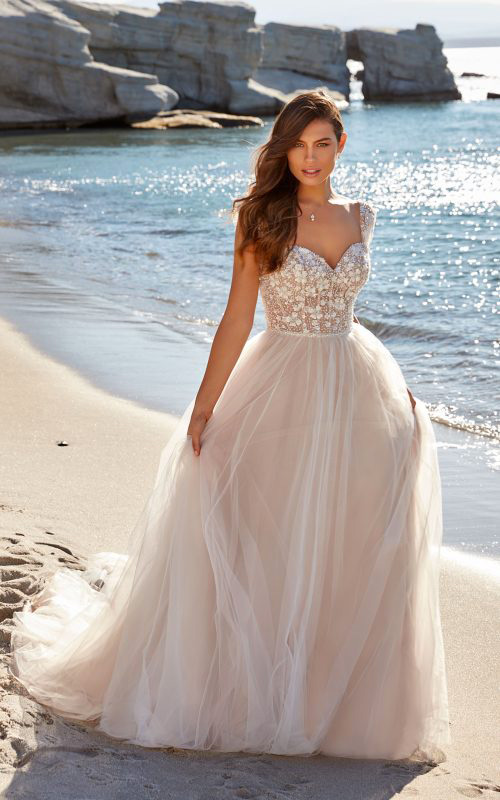 In questa foto una modella in riva al mare indossa un abito da sposa Eddy K 2023 
