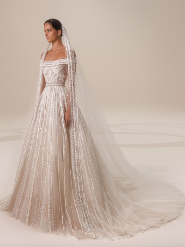 In questa foto una modella indossa un abito da sposa con inserti luminosi e scollatura a barca della collezione autunno di Elie Saab 2023