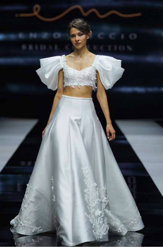 In questa foto una modella sfila sulla passerella con un vestito da sposa crop top della collezione Enzo Miccio Bridal 2023