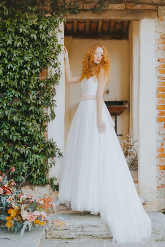 In questa foto una modella sul ciglio di una porta posa con un abito da sposa con cintura rosa in vita della collezione Giuliani Couture 2023